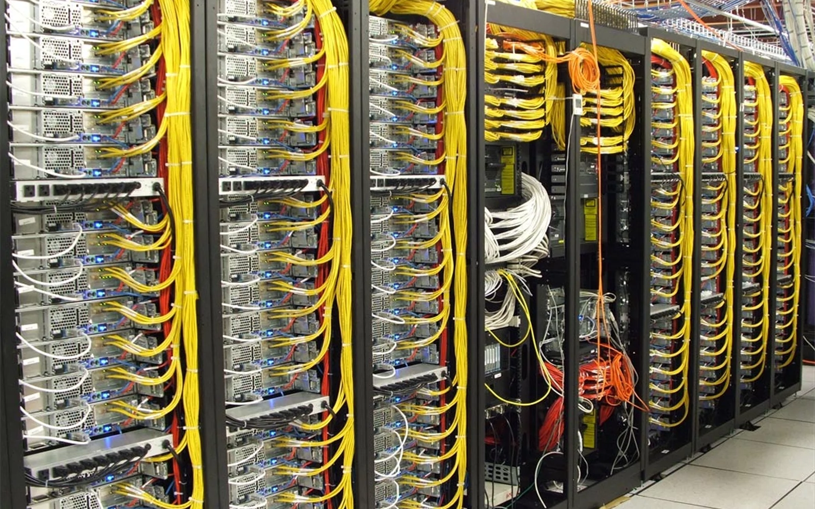 Åpne serverrack med teknisk utstyr og gule, hvite og oransje kabler.