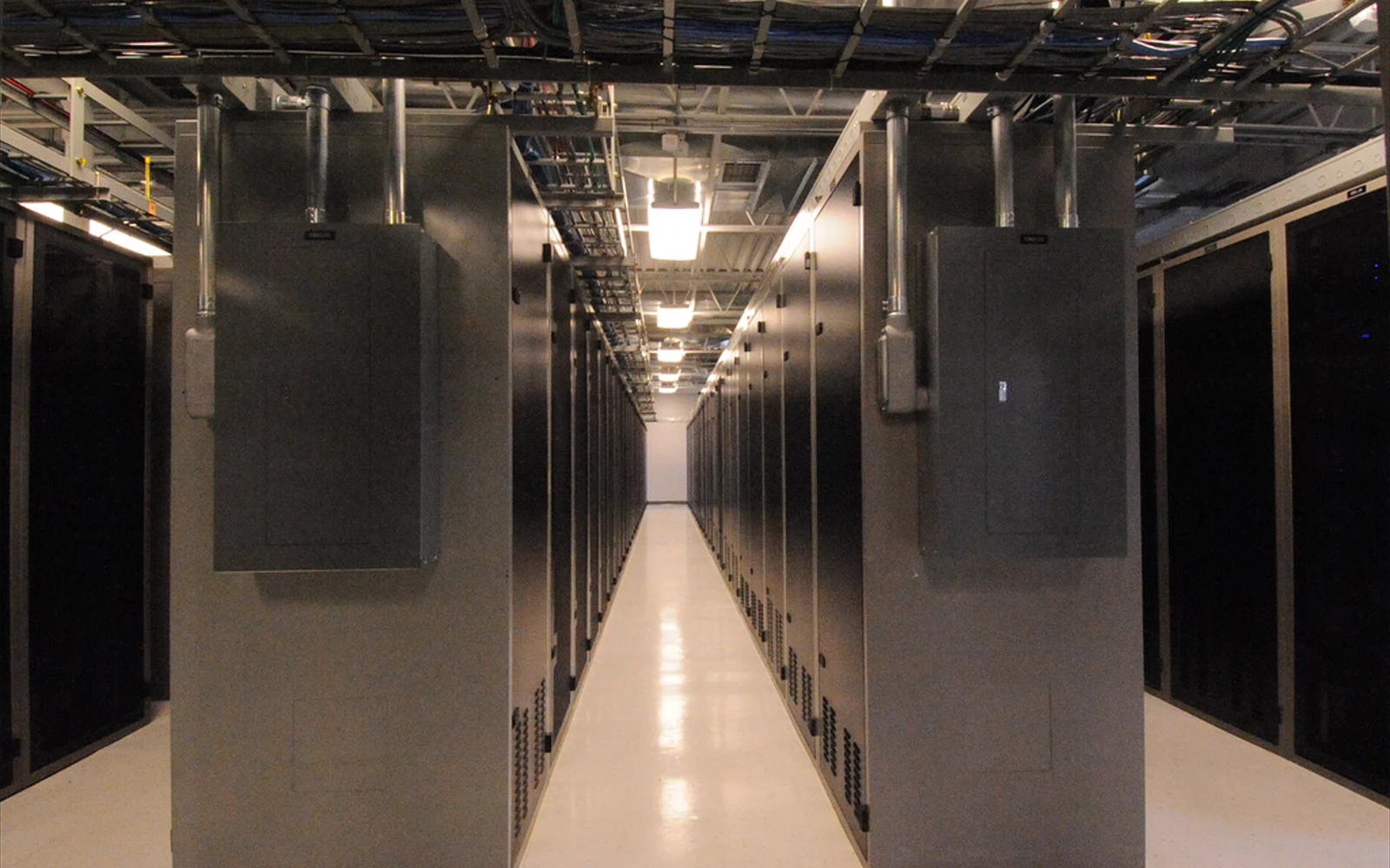 Lang gang mellom mørke serverrack, med kabelbroer i taket.