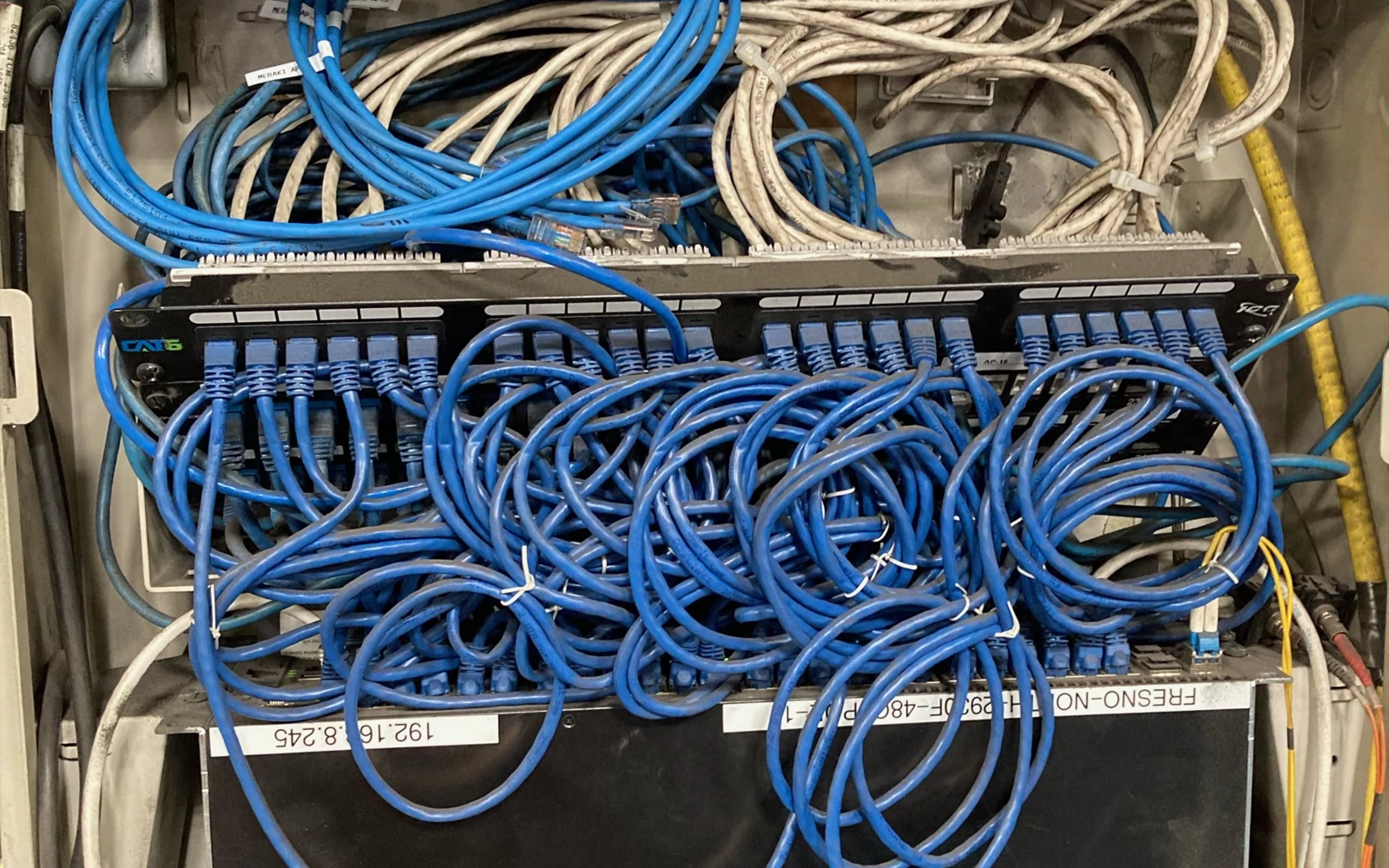 Nettverksskap med svitsjer, patchpaneler og mange blå og lyse kabler.