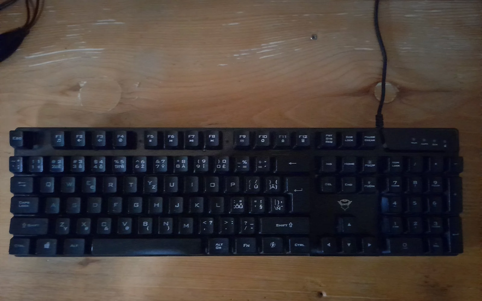 Svart datatastatur med tallfelt og kabel på et trebord.