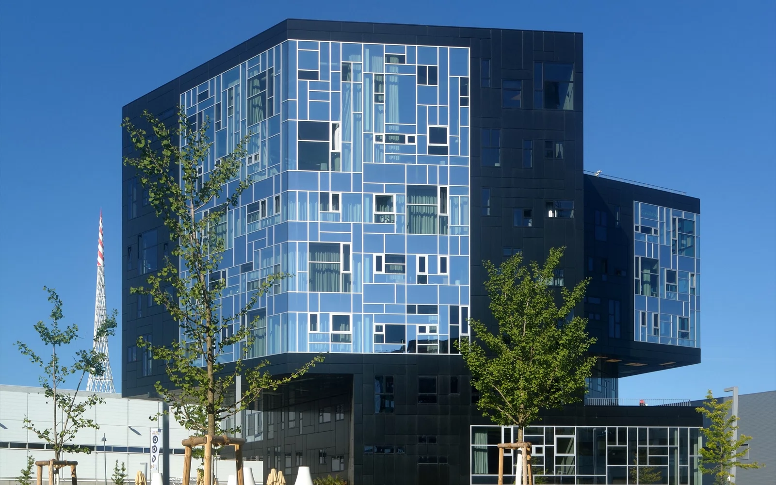 Moderne universitetsbygg med blå glassfasade og unge trær.