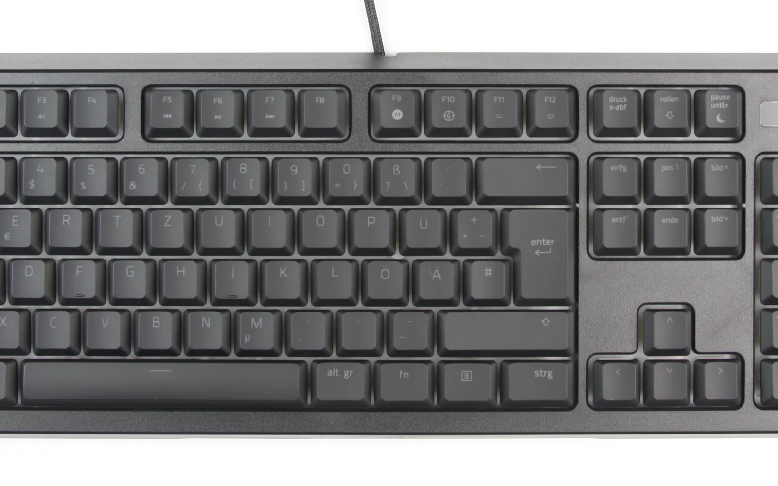 Mørkt tastatur med avrundede taster og kabel mot lys bakgrunn.