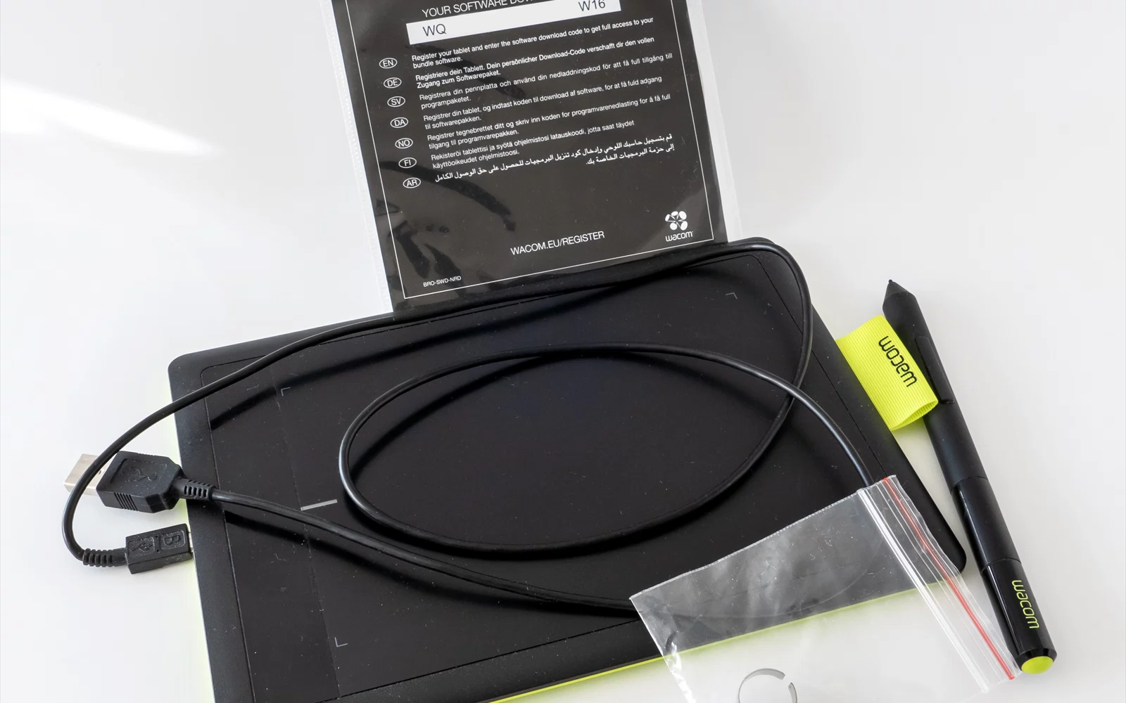 Svart tegnebrett med kabel, penn, dokumentasjon og tilbehør på hvit bakgrunn.