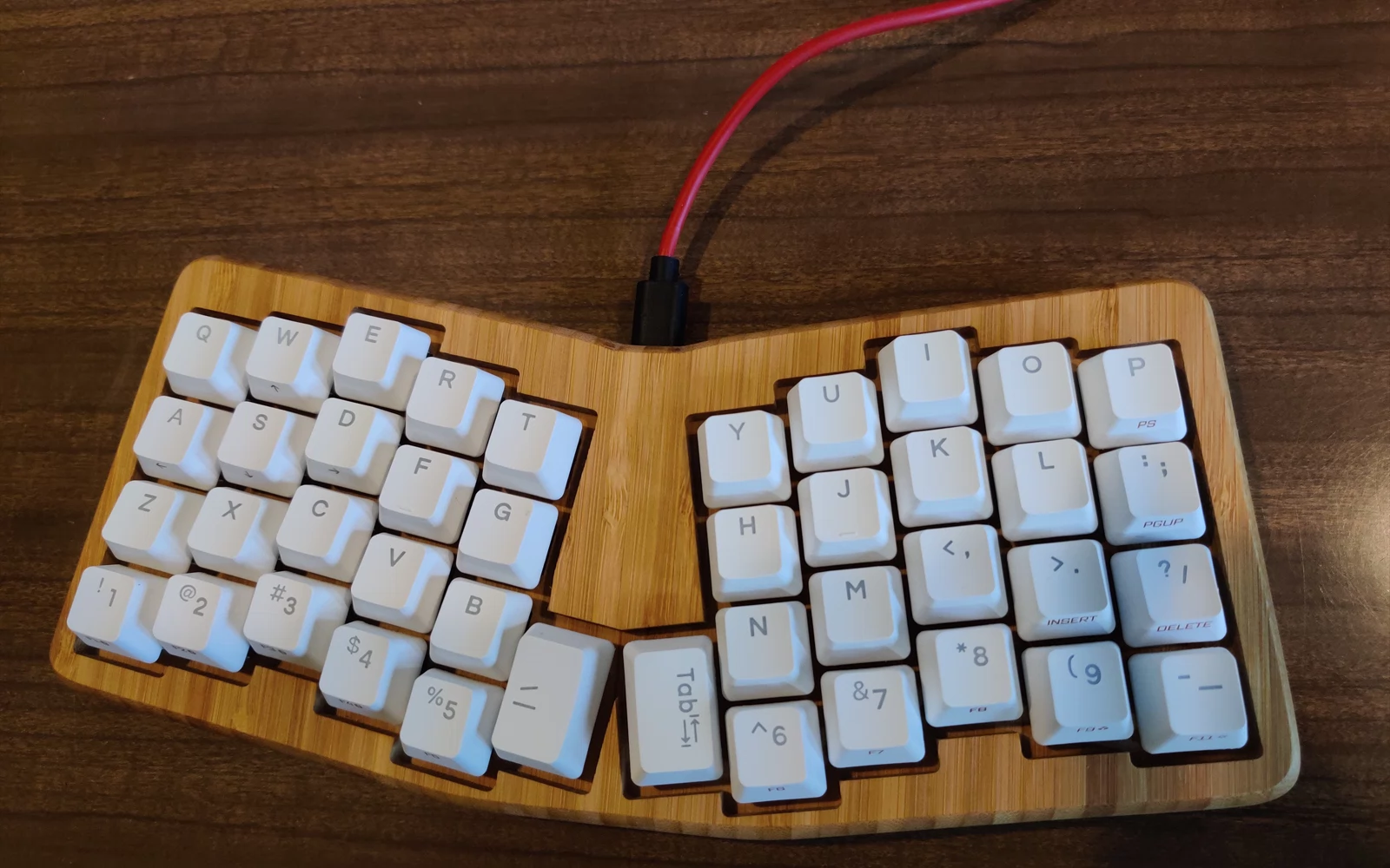 Kompakt ergonomisk tastatur med hvite taster i trekabinett og rød kabel.